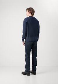 Pullover a coste navy con maniche lunghe, abbinato a jeans blu scuro e scarpe nere. La texture del pullover è evidente e lavorata.