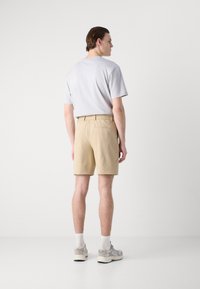 Pantalones cortos beige con un diseño texturizado y dos bolsillos traseros, combinados con una camiseta de cuello redondo gris claro y calcetines tobilleros blancos.