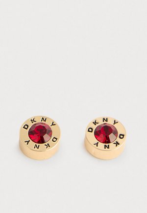 Orecchini a perno rotondi dorati con gemme rosse al centro e "DKNY" inciso in nero lungo i bordi, mostrati su uno sfondo bianco.