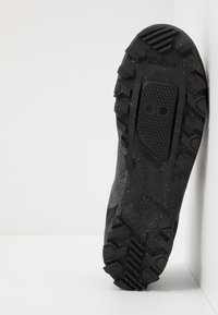 Černá turistická obuv s texturovanou gumovou podrážkou s hlubokými výstupky a hexagonálními vzory; svršek je vyroben z odolného tmavého materiálu.