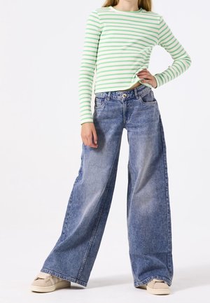 Un haut à rayures vertes et blanches à manches longues, associé à un jean en denim bleu à jambes larges. Le jean est doté d'une fermeture à bouton et de poches avant.