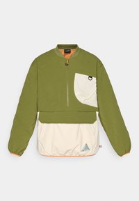 Chaqueta de pullover verde y crema con cremallera de cuarto de longitud, textura acolchada, puños elásticos y un logo triangular en el dobladillo inferior.