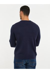 Marineblauwe gebreide trui met een ronde hals en ribgebreide manchetten en onderrand. Gemaakt van een zachte stof, iets getailleerd met een gladde textuur.