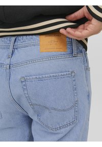 Ljust blå denimjeans med en läderlogotyp på baktyget, synlig sömnad och standard bakfickor.