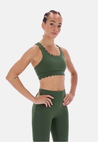 Ciemnozielony sportowy stanik i legginsy z wysokim stanem z falistymi krawędziami i bezszwowym wzorem, wykonane z elastycznego, gładkiego materiału.