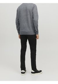 Pull tricoté à pois bleus, pantalon noir coupe slim et baskets noires avec des accents blancs. Vue de dos, mettant en valeur le design global de la tenue.