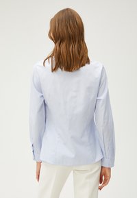 Lyseblå stribet skjorte med lange ærmer, skræddersyet pasform og knaplukninger ved ærmerne. Cottonblanding med en glat tekstur og subtil glans.
