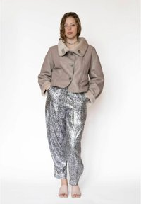 Lichtgrijs leren cropped jack met een grote kraag en bontafwerking. Zilveren broek met slangendessin en lichtroze open sandalen met open teen.