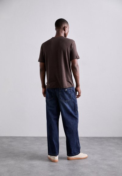 Brun kortärmad t-shirt matchad med avslappnat passande mörkblå jeans. Jeansen har en klassisk femficksdesign och subtila sömnadsdetaljer.