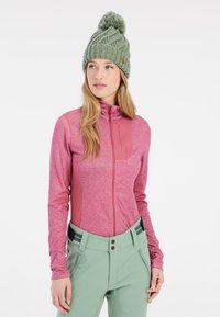 Giacca rosa aderente con zip, dalla finitura texturizzata e pannelli bordeaux, abbinata a pantaloni verde chiaro con una finitura liscia e dettagli con bottoni.