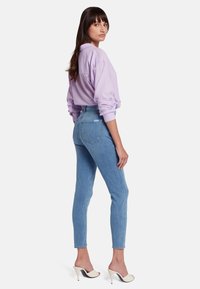 Jean slim en denim bleu clair, taille haute, avec cinq poches et une finition soignée. Associé à une chemise pastel violette.