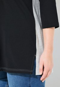 Maglietta a maniche corte nera e grigia chiara con design a pannelli laterali e cuciture in vista, abbinata a jeans blu.