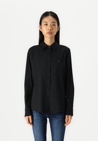 Zwarte lange mouw button-up shirt met een gestructureerde kraag, voorzien van een klein logoaccent op de borst en een gladde stoftextuur.