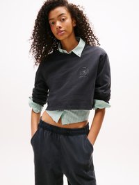Sort cropped sweatshirt med logo, lagd over en grøn og hvid stribet skjorte. Mørkeblå sweatpants med elastisk talje og lommer.