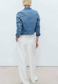 Lysblå denimjakke i cropped stil med en frontlomme, knaplukning og opbrudte ærmer, sat sammen med hvide vide bukser.