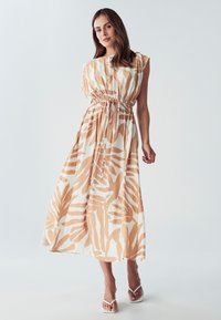 Volnější šaty z lehkého materiálu, zdobené béžovým a bílým vzorem listů, s nabíraným pasem a krejčovským střihem až k kotníkům.