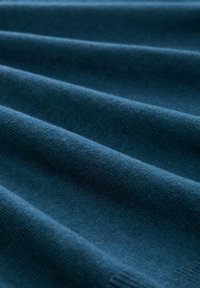 Dunkelblauer Stoff mit einer glatten Textur, der horizontale Falten und ein feines Strickmuster aufweist, was Weichheit und Farbentiefe zeigt.