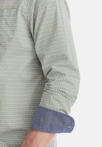 Hemd mit einem strukturierten grünen und weißen Muster, das mit einem blauen Denim-Bund und einer Brusttasche versehen ist. Lange Ärmel und eine taillierte Passform.