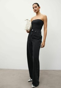 Svarta högmidjade jeans med vida ben, kombinerat med en figursydd svart strapless topp. Håller en liten vit väska och bär glänsande silverfärgade spetsiga klackar.