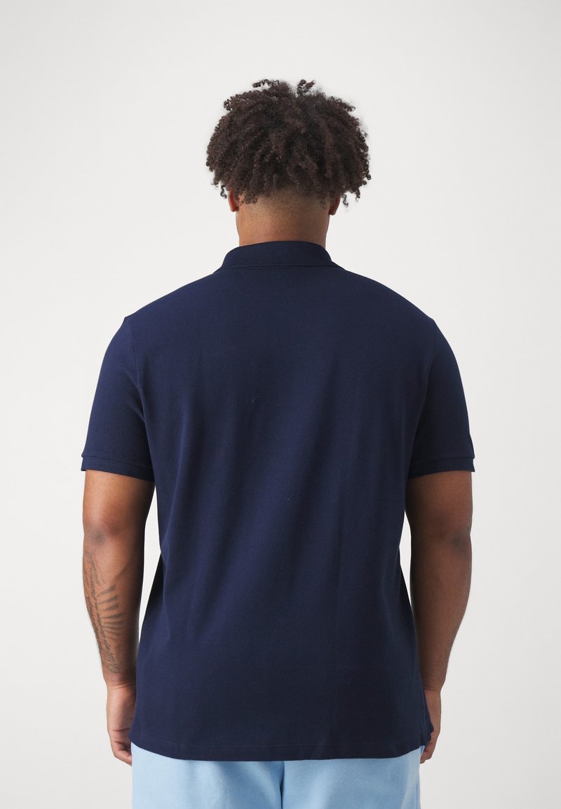 Polo bleu marine avec un col classique, des manches courtes et un tissu texturé. La vue de dos montre une finition lisse et des fentes latérales.