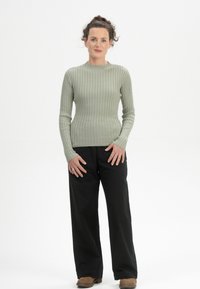 Hellgrünes, geripptes Langarmshirt, kombiniert mit lockeren, schwarzen Hosen und braunen Schuhen. Einfaches Design mit rundem Halsausschnitt und taillierter Passform.