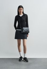 Polo a maniche lunghe nera, gonna in denim scuro e borsa a tracolla nera con borchie metalliche. Calzettoni bianchi alla caviglia e sneakers nere completano l'outfit.