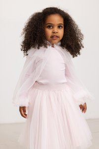 Lys rosa kjole med ribbet liv, tyllskjørt og gjennomsiktige kappe-ermer med volanger. Enkelt, elegant design med en myk tekstur.