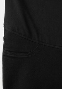 Zbliżenie na czarną tkaninę z widocznym szwem i częściowym detalem kieszeni, podkreślające fakturę i przeszycia.