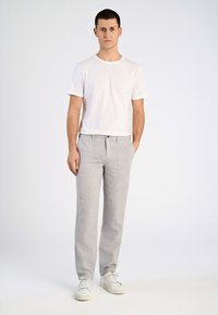 Witte t-shirt met korte mouwen in combinatie met lichtgrijze gestreepte broek, met een ontspannen pasvorm en voorzakken. Gemaakt met witte sneakers.