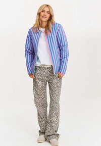 Padded jacket w pionowe różowe i niebieskie paski, zestawiony z spodniami w panterkę o rozszerzanym fasonie. Neutralna bluzka pod spodem, jasne buty.