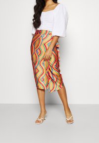 Jupe colorée et à motifs avec des motifs en vagues dans des teintes vives. Fabriquée en matériau lisse, de longueur intermédiaire avec une fente sur le côté, associée à des talons blancs.