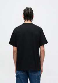 Czarny bawełniany t-shirt z okrągłym dekoltem i krótkimi rękawami, o luźnym kroju i gładkiej teksturze. Widoczne szwy na ramionach.