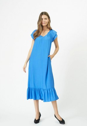 Vestido midi de manga corta y escote en V en un brillante tejido azul. Presenta un escote fruncido, bolsillos y un dobladillo con volantes. Se llevan unos tacones altos negros.