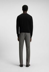 Black sweater with a crew neckline, paired with gray tailored pants, shown from behind against a neutral background. Smooth texture, slim fit.