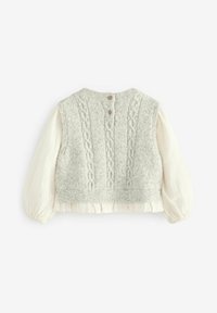 Gilet en tricot gris avec un motif en maille torsadée, doté d'un col rond et de boutons décoratifs à l'arrière, superposé sur une blouse blanche à texture.