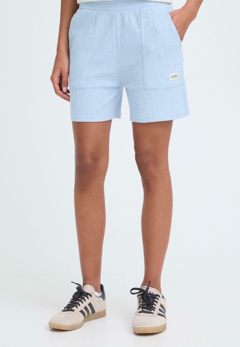 Shorts en coton tissé bleu clair avec une taille élastique et deux poches latérales. Présente une petite étiquette logo sur la poche avant.