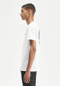 Camiseta de algodón blanca con mangas cortas y un logo negro en la parte superior de la espalda, combinada con leggins negros con estampado.