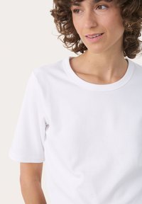 Hvid bomulds t-shirt med rund hals og korte ærmer. Stoffet har en glat tekstur med subtile sømdetaljer på ærmerne.