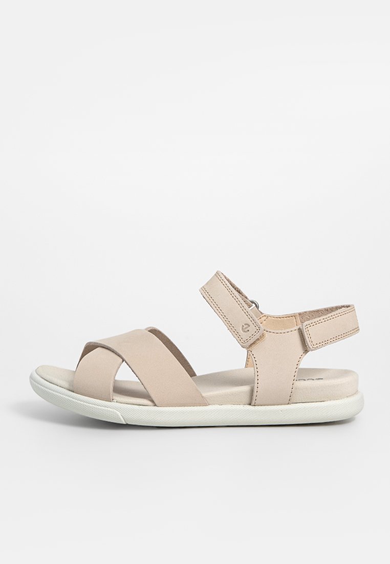 Beige Sandale mit Überkreuzriemen aus weichem Material. Verstellbarer Knöchelriemen mit Klettverschluss. Gepolsterte Innensohle und Gummisohle.