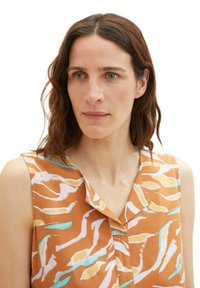 Sleeveless top in orange fabric with abstract multicolored patterns. Features a v-neck and subtle button details along the front.