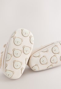 Zachte babyschoentjes met witte zolen, waarop een herhalend patroon van eenvoudige beige berengezichten op de onderkant is afgebeeld.