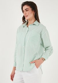 Lightweight, green and white striped button-up shirt with a collar, two chest pockets, and long sleeves. Fabric appears smooth and slightly sheer.