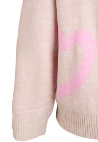 Beežist kootud kampsunisärk, millel on soonikkoes varrukasäär ja osaliselt nähtav roosa südame muster pehmel kangal.