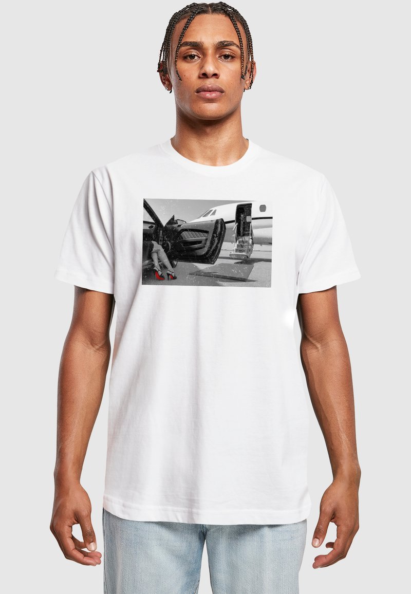 White cotton t-shirt featuring a black-and-white photographic print of a leg in red heels by a sleek aircraft door.