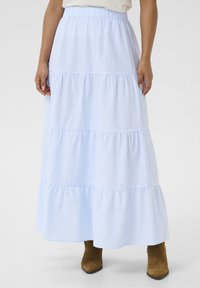 Jupe mi-longue bleu clair à volants avec des rayures blanches, taille élastique et ourlet à volants. Portée avec des bottines brunes.