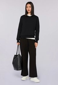 Svart sweatshirt med rund hals, kombinerad med vida svarta byxor. Texturerad svart väska med handtag. Vita sneakers fulländar outfiten.