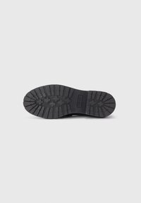 Black rubber boot sole with a textured tread pattern and logo, featuring grooves for traction and stability. Flat, rounded toe design.