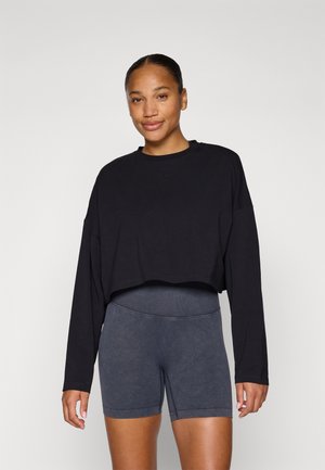 Schwarzes, tailliertes Langarmshirt aus weichem Material, kombiniert mit hochgeschnittenen, dunkelgrauen Shorts, die eine glatte Textur und eine enganliegende Passform aufweisen.