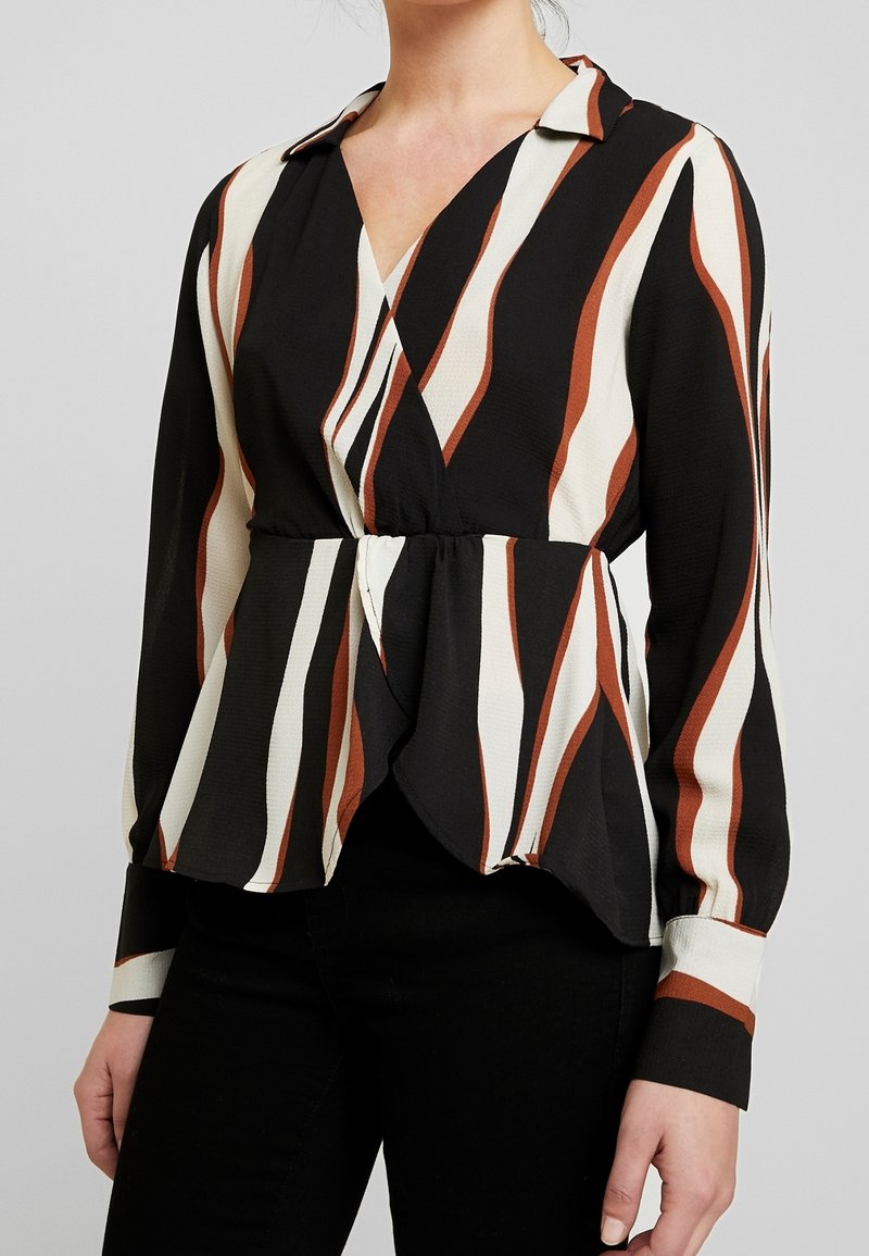 Blusa a righe bianco e nere con dettagli marroni, caratterizzata da un design avvolgente, maniche lunghe e un dettaglio in vita a peplo.