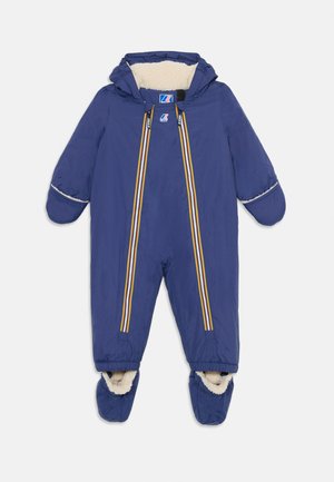 Combinaison de neige une pièce bleu marine avec capuche, doublée de fausse fourrure crème. Présente deux zips avant avec des rayures colorées et des chaussons.
